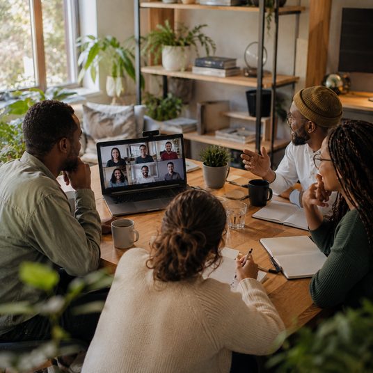 Four people around a laptop on a video call with remote teammates