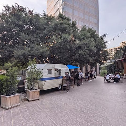 Coffee trailer under live oaks on an Austin plaza with people at outdoor tables