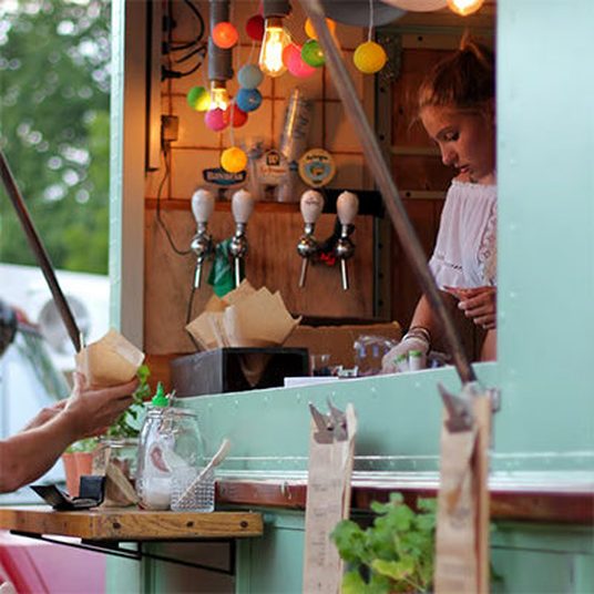 Server pouring drinks at a mint green food truck strung with lights