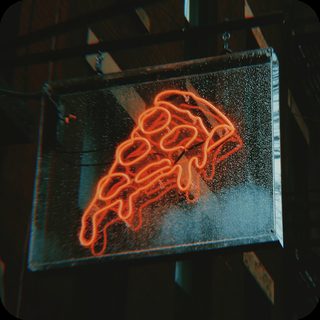 Neon pizza slice sign glowing outside a New York pizzeria
